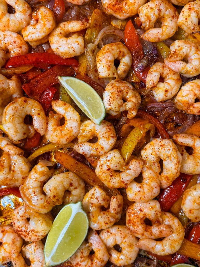 Sheet Pan Shrimp Fajitas cooked with red and yellow bell peppers and onions, seasoned with spices, and garnished with two lime wedges.