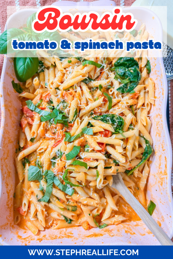 Baked Boursin Cheese Pasta features penne smothered in a creamy tomato sauce, fresh spinach, and rich Boursin cheese, all garnished with fragrant basil. A wooden spoon rests in the dish, with grated cheese sprinkled on top for the perfect finishing touch.