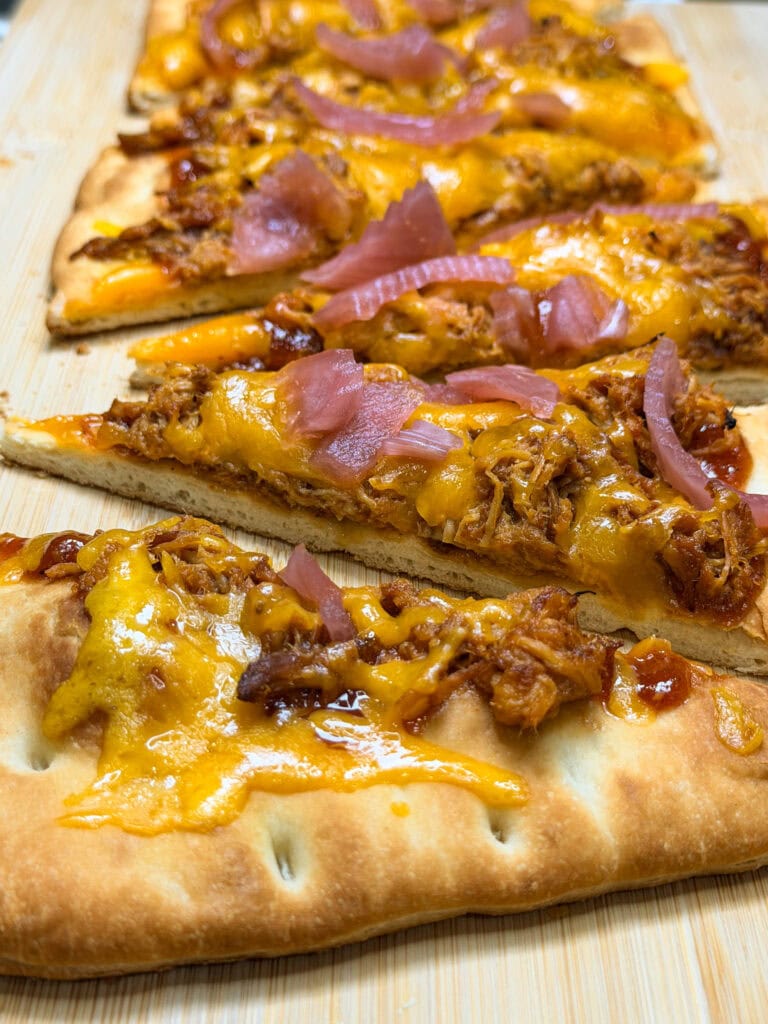 Flatbread slices topped with melted cheddar cheese, tender Crock Pot BBQ Chicken, and pickled red onions, served on a wooden board.
