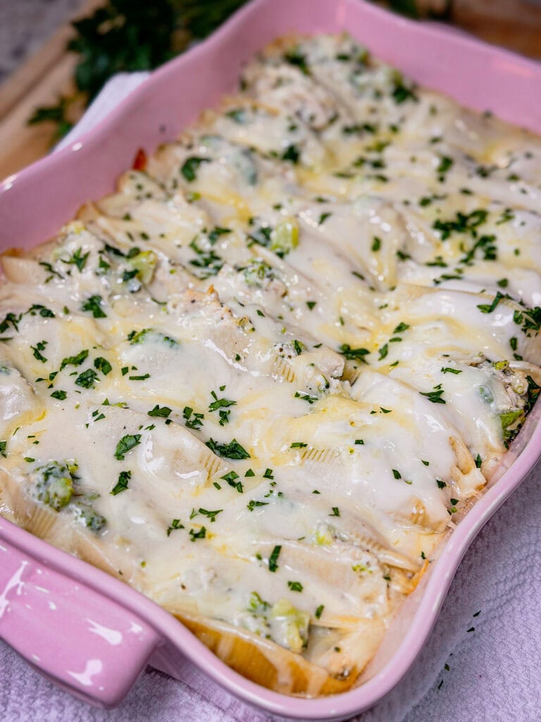 A pink baking dish filled with Chicken Alfredo Stuffed Shells, topped with melted cheese and sprinkled with chopped parsley.