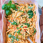Baked Boursin Cheese Pasta with penne in a creamy tomato sauce and spinach, topped with fresh basil and grated cheese, served in a pink casserole dish with a wooden spoon.