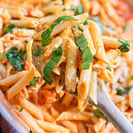 A close-up of creamy Baked Boursin Cheese Pasta with tangy tomato sauce, fresh basil, and melted cheese on a wooden spoon, with more pasta in the background.