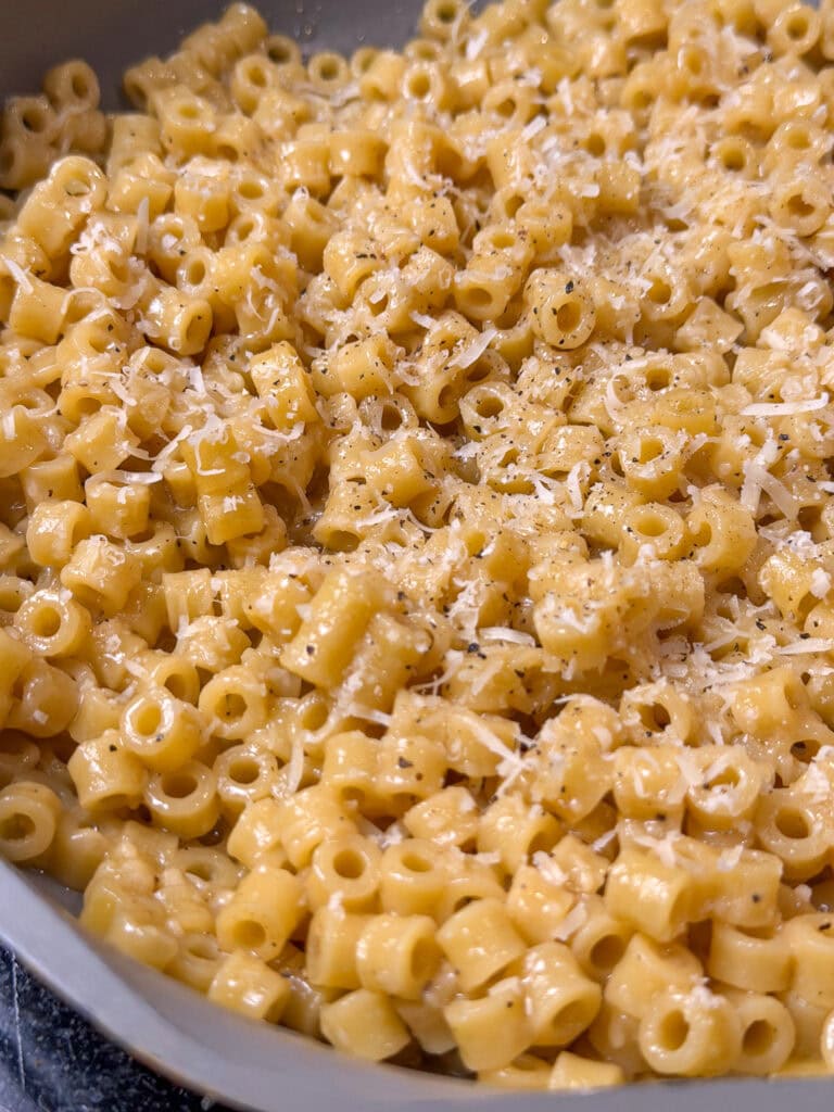 A close-up of cooked ditalini pasta mixed with grated cheese and black pepper, reminiscent of The Best Buttered Noodles, creates a creamy, cheesy dish.