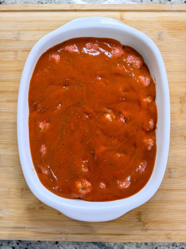 A white oval baking dish filled with shrimp covered in a thick, seasoned red tomato sauce sits on a wooden cutting board, reminiscent of the hearty comfort found in classic Porcupine Meatballs.