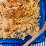 Creamy Chicken and Rice Casserole features baked chicken breasts seasoned with spices, nestled on a bed of creamy rice and mushrooms in a blue glass baking dish, with a wooden spoon on the side.