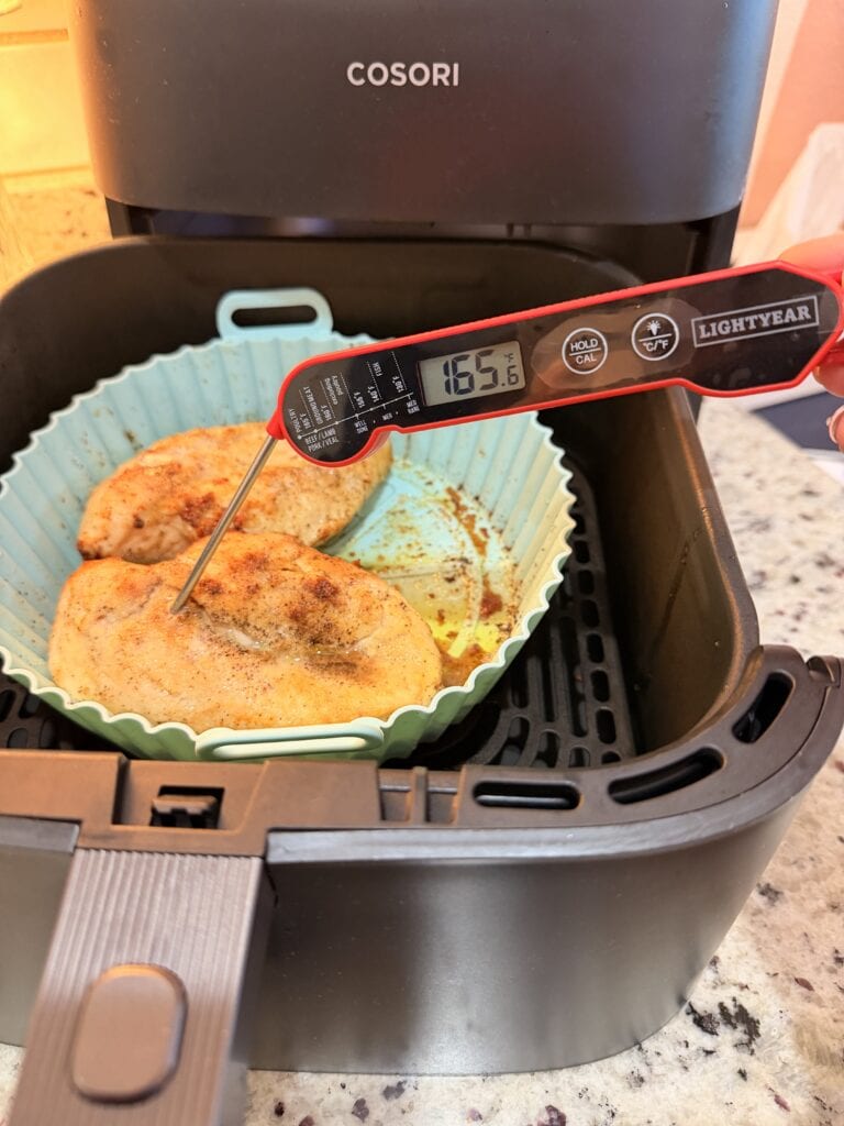 A digital thermometer shows 165.6°F while checking cooked chicken breasts for Air Fryer Chicken Quesadilla in a silicone tray inside a COSORI air fryer on a kitchen counter.