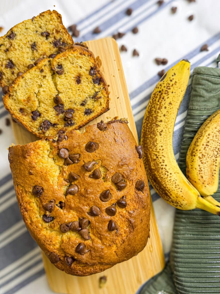 sliced banana bread with chocolate chips on a wood cutting board with bananas in the background