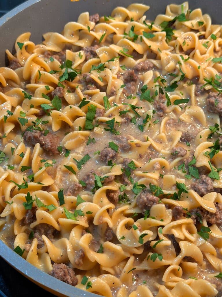 A skillet filled with cooked egg noodles, ground beef, creamy sauce, and garnished with chopped fresh parsley—just like a classic Homemade Hamburger Helper Beef Stroganoff.