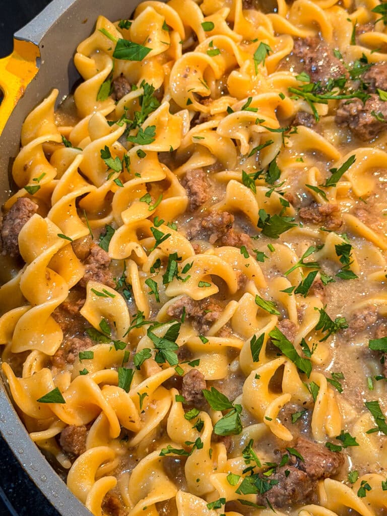 A close-up of a skillet filled with cooked egg noodles, ground beef, and creamy sauce, garnished with chopped fresh parsley—just like a classic Homemade Hamburger Helper Beef Stroganoff.