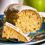 Golden brown apple cider Bundt cake drizzled with cider glaze and sprinkled with cinnamon sugar on a white cake stand.