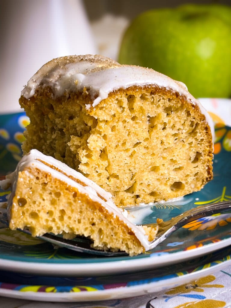 Golden brown apple cider Bundt cake drizzled with cider glaze and sprinkled with cinnamon sugar on a white cake stand.