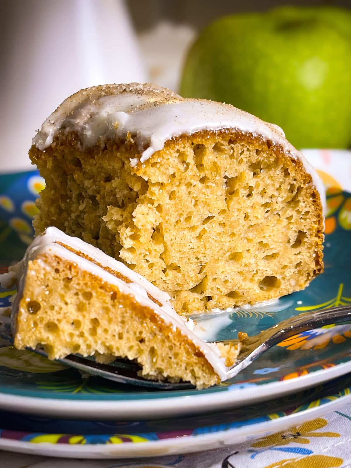 Golden brown apple cider Bundt cake drizzled with cider glaze and sprinkled with cinnamon sugar on a white cake stand.