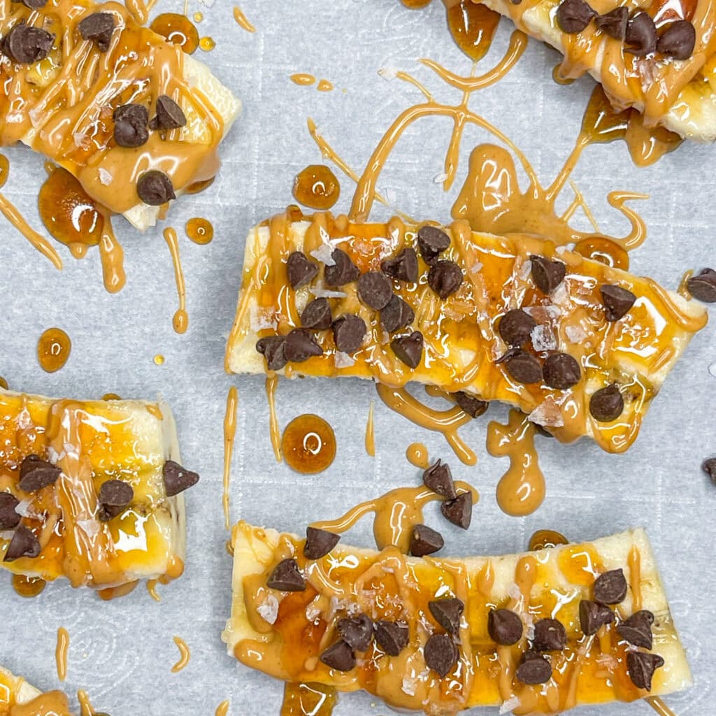 Frozen Banana Treats: Sliced bananas on parchment paper, topped with drizzled caramel sauce and sprinkled with chocolate chips.