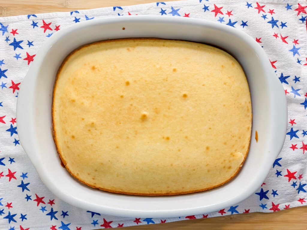A golden-brown Patriotic Jell-O Poke Cake in a white dish sits on a cloth decorated with red and blue stars.