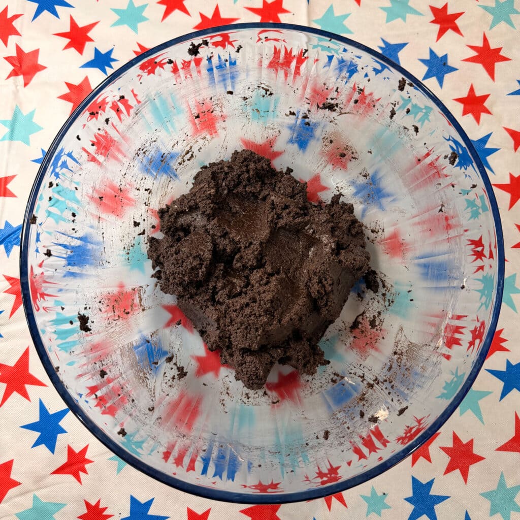 A clear glass bowl filled with a mound of Patriotic Oreo Truffles sits on a table covered with a red, white, and blue star-patterned tablecloth.