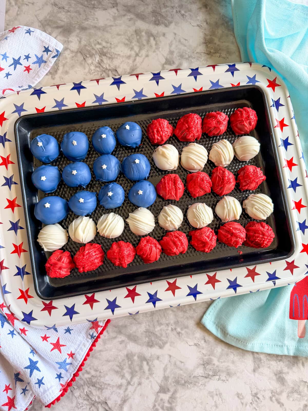 A tray of Patriotic Oreo Truffles decorated in blue, red, and white to resemble the American flag, with blue truffles featuring white stars and alternating rows of red and white, all displayed on a star-patterned tray.