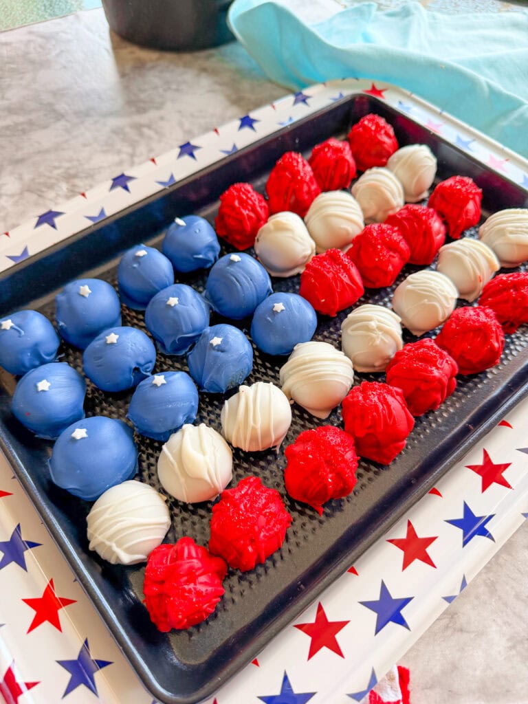 A tray of Patriotic Oreo Truffles decorated in blue, white, and red to resemble the American flag, with blue truffles topped with white stars, arranged on a star-patterned tray.