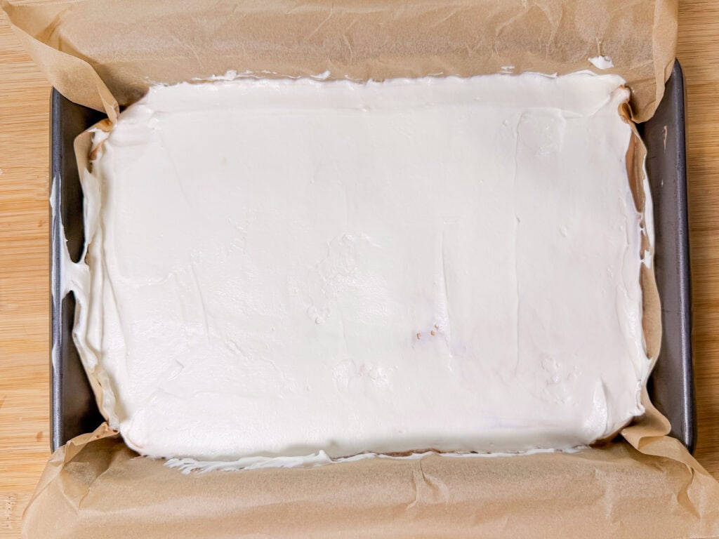 A rectangular baking pan lined with parchment paper holds a smooth layer of white marshmallow mixture, perfect for making Frozen S’mores or cutting into squares for your next sweet treat.