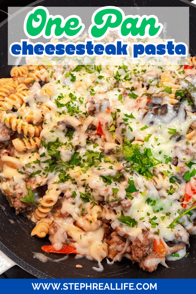 A skillet filled with One Pan Cheesesteak Pasta made with rotini, ground beef, melted cheese, and colorful peppers, garnished with chopped parsley. Text on image reads One Pan Cheesesteak Pasta and www.stephreallife.com.