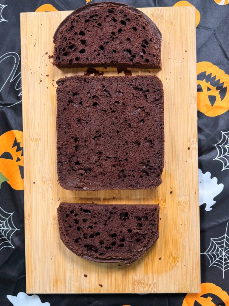 Three slices of chocolate bread on a wooden cutting board, set atop a Halloween-themed tablecloth with pumpkins, spiders, and webs—perfect inspiration for your 10 Easy Halloween Ideas.