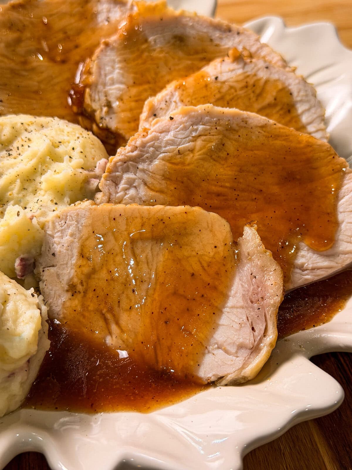 Slices of roasted pork or crock pot turkey with cranberry, topped with gravy next to a serving of mashed potatoes on a plate.