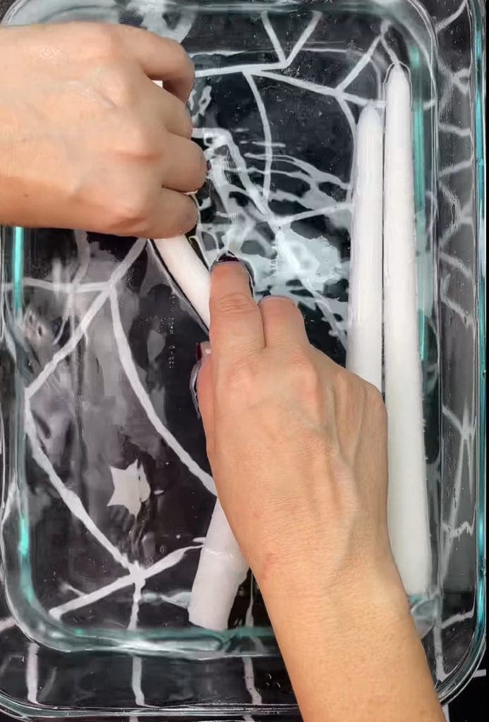 Two hands shape white candles in a glass dish filled with water; a spiderweb pattern is visible beneath the dish, making this one of 10 Easy Halloween Ideas for adding a spooky touch to your decor.