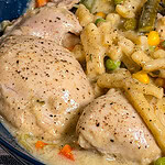 Crock Pot Chicken and Noodles features tender chicken thighs in a creamy sauce with macaroni noodles, mixed vegetables including corn, carrots, peas, and green beans, all served in a blue bowl.