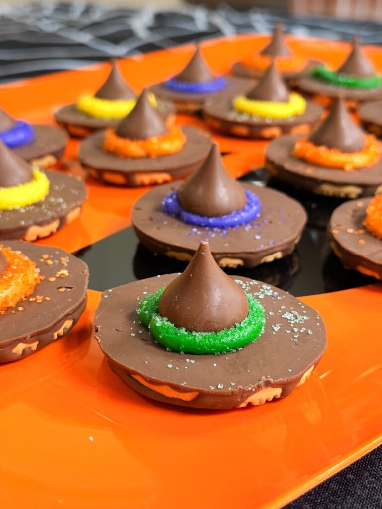 Chocolate cookies decorated as witch hats, topped with chocolate kisses and colorful sugar rings, arranged on an orange tray—perfect for adding to your list of 10 Easy Halloween Ideas.