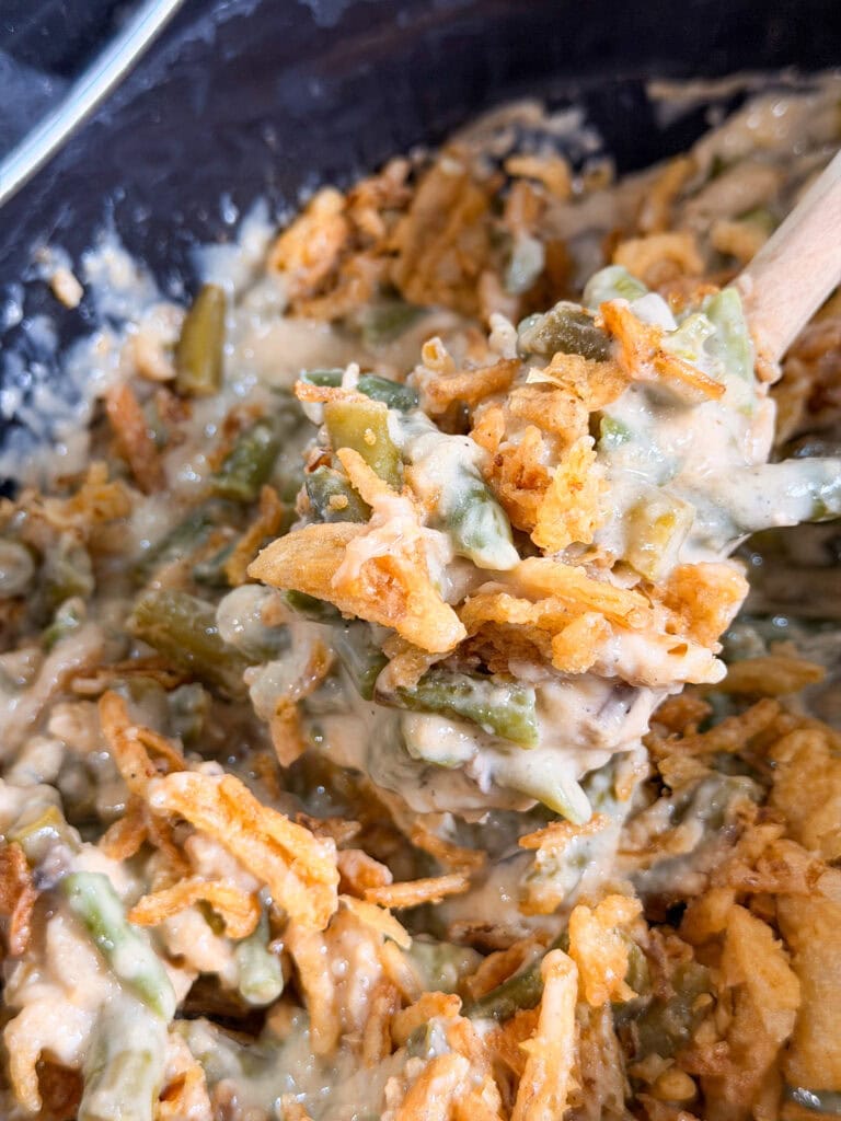 Close-up of a spoon lifting green bean casserole, featuring a Monster Mix of crispy fried onions, creamy sauce, and tender green beans.