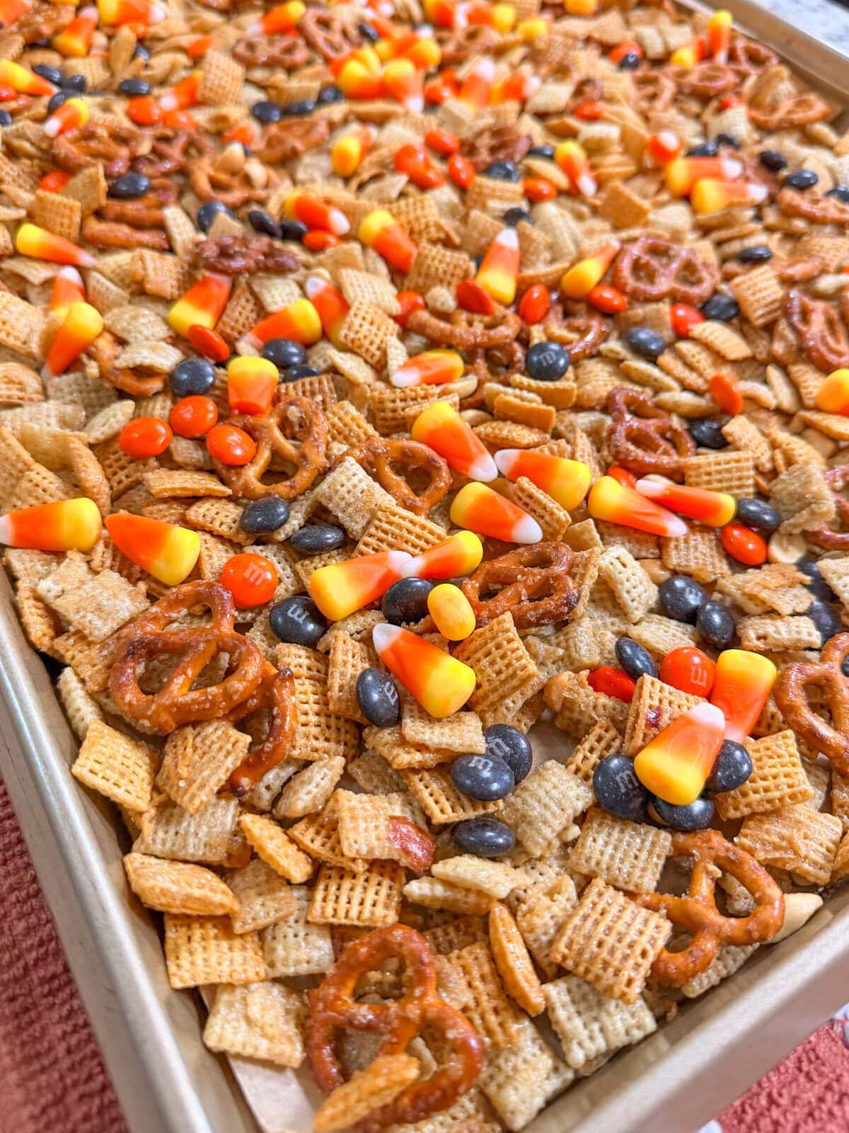 A baking sheet filled with a Monster Mix snack of Chex cereal, pretzels, candy corn, peanuts, and chocolate candies.