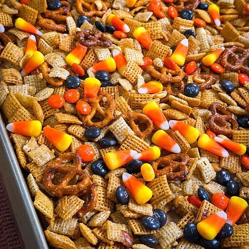 A close-up of Monster Mix snack featuring a delicious medley of pretzels, Chex cereal, candy corn, peanuts, and chocolate candies on a baking sheet.
