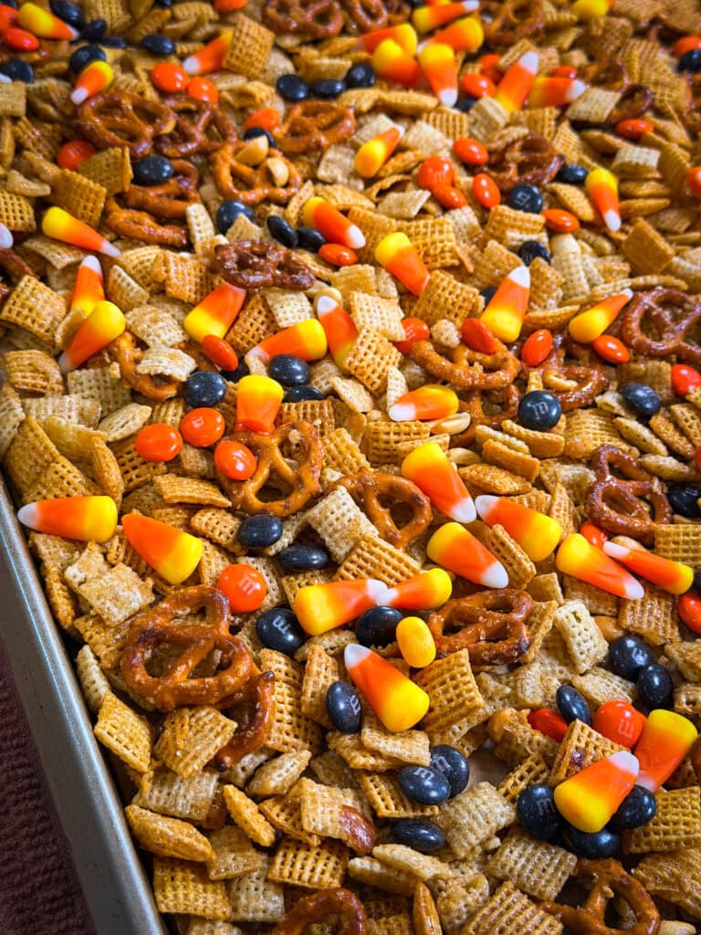 A close-up of Monster Mix snack featuring a delicious medley of pretzels, Chex cereal, candy corn, peanuts, and chocolate candies on a baking sheet.