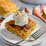 Squares of Pumpkin Cheesecake Bars on a white plate, topped with whipped cream and sprinkled with cinnamon.