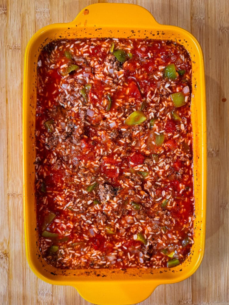A yellow baking dish filled with a delicious Stuffed Pepper Casserole—a hearty mixture of rice, ground meat, green bell peppers, and tomato sauce—sits invitingly on a wooden surface.
