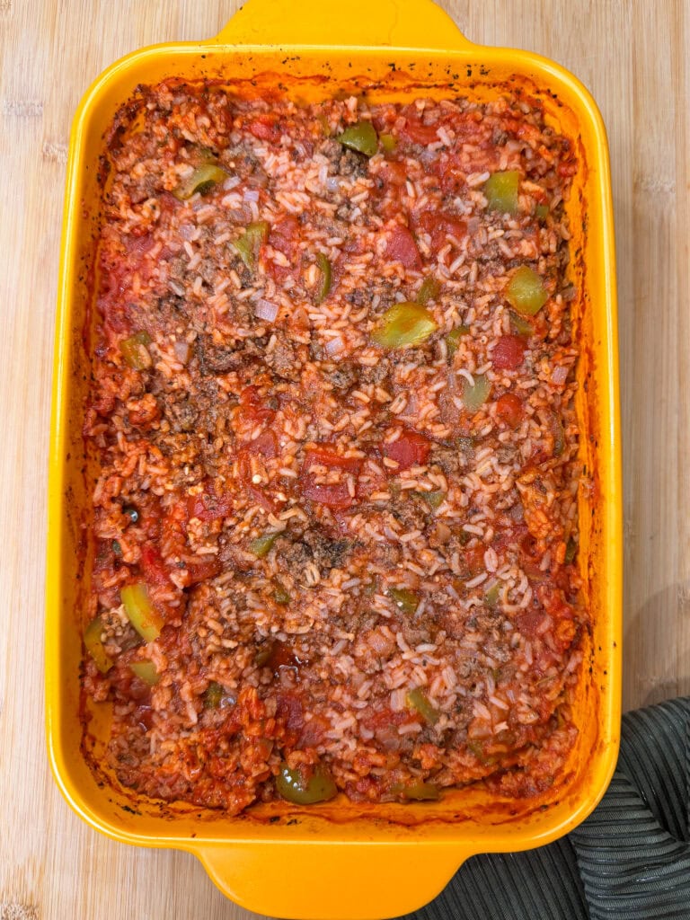 A yellow baking dish filled with a delicious Stuffed Pepper Casserole made of rice, ground meat, diced tomatoes, green bell peppers, and onions. The casserole is slightly browned around the edges.