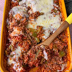 A yellow baking dish filled with a cheesy Stuffed Pepper Casserole of rice, ground meat, tomato sauce, green bell peppers, and melted cheese, being served with a wooden spoon.
