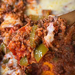 A wooden spoon holds a scoop of cheesy Stuffed Pepper Casserole with ground beef, rice, diced tomatoes, green bell peppers, and melted cheese, with more casserole visible in the background.