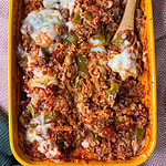 A yellow baking dish filled with a cheesy Stuffed Pepper Casserole made of rice, ground beef, green bell peppers, tomato sauce, and melted cheese, with a wooden spoon scooping some out.