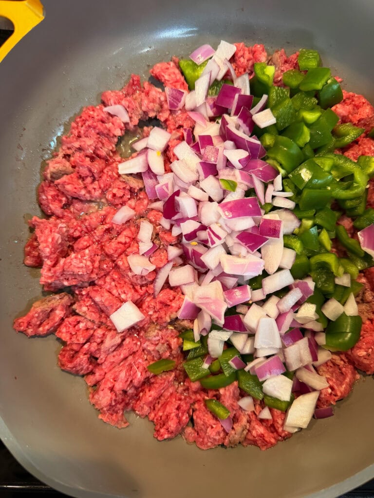 Ground beef, chopped red onions, and green bell peppers sizzle together in the pan, creating a flavorful base for a hearty Taco Skillet.