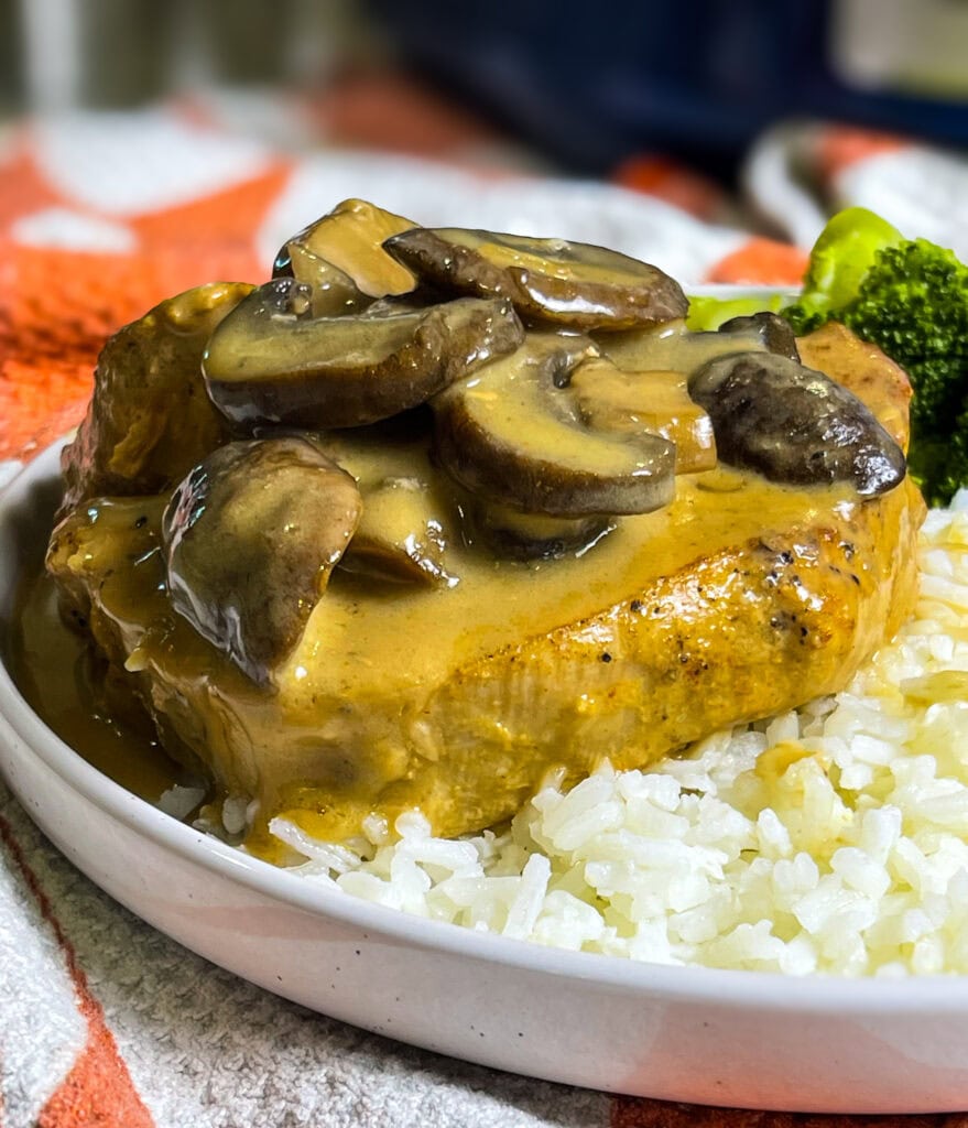 Slow Cooker Mushroom Pork Chops served on a plate with creamy mushroom gravy spooned over top, alongside mashed potatoes and green beans.