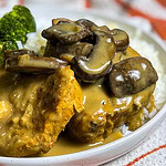 Slow Cooker Mushroom Pork Chops served on a plate with creamy mushroom gravy spooned over top, alongside mashed potatoes and green beans.
