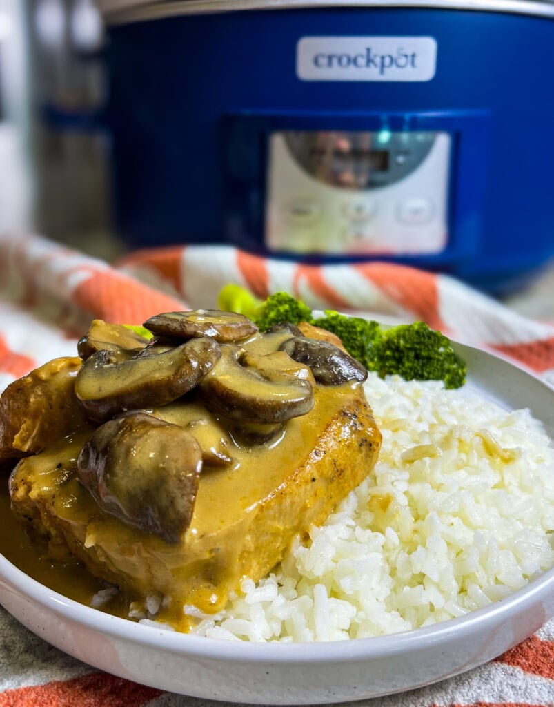 Slow Cooker Mushroom Pork Chops served on a plate with creamy mushroom gravy spooned over top, alongside mashed potatoes and green beans.