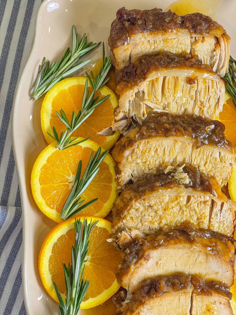 Tender pork loin cooked in a crock pot with apples, onions, cranberry sauce, fresh orange zest, and rosemary, sliced and served with a rich cranberry orange gravy for a festive slow cooker holiday dinner.