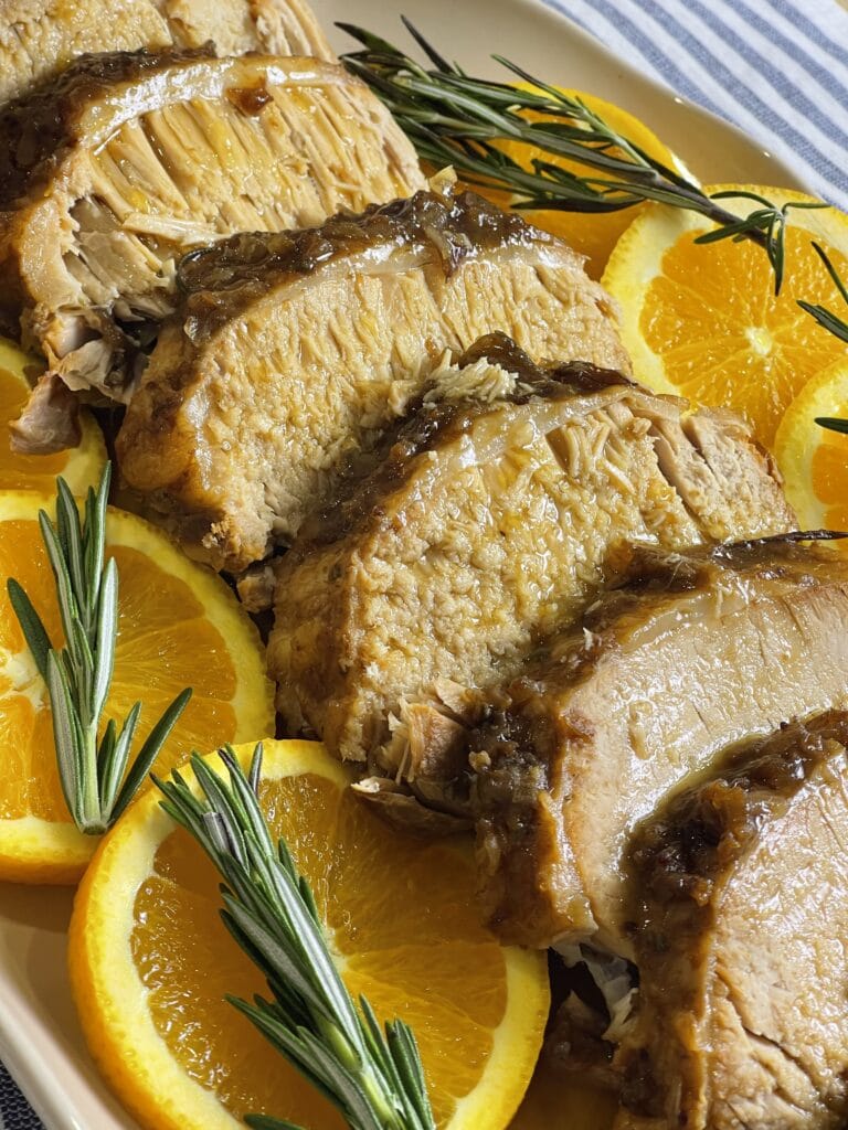 Tender pork loin cooked in a crock pot with apples, onions, cranberry sauce, fresh orange zest, and rosemary, sliced and served with a rich cranberry orange gravy for a festive slow cooker holiday dinner.