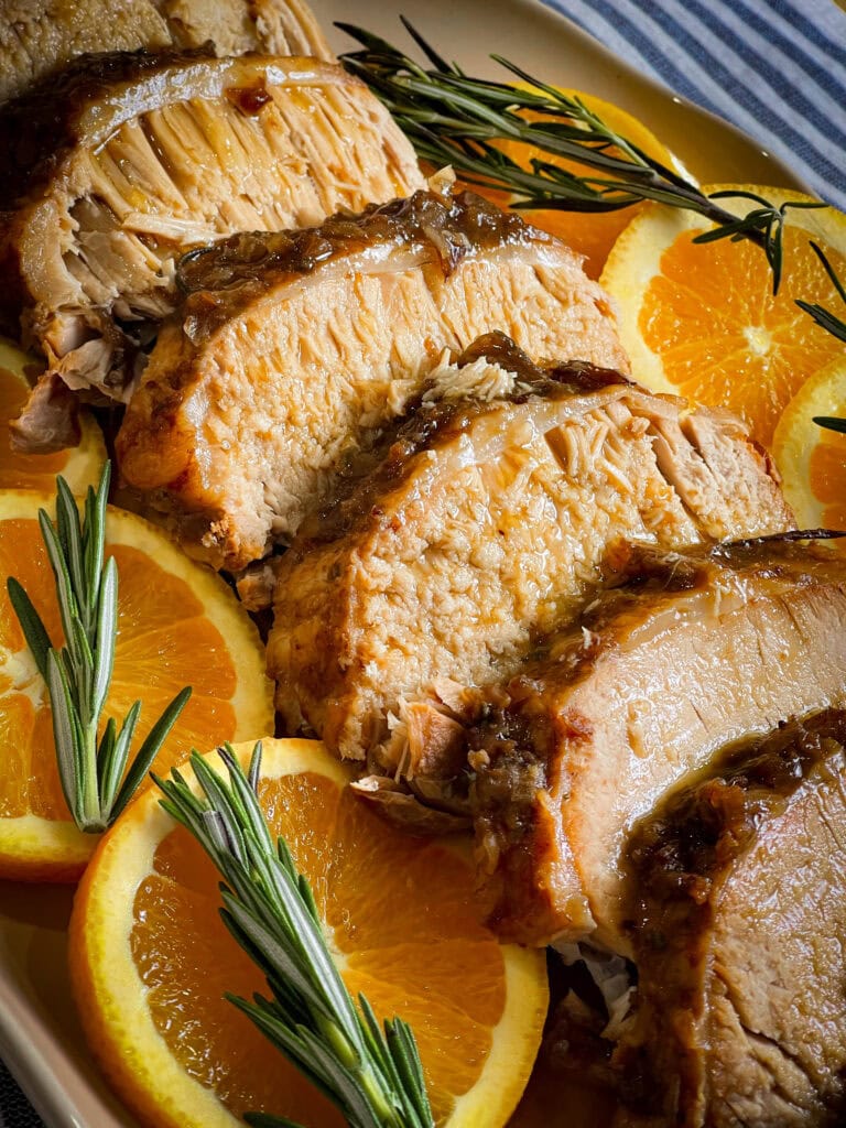 Tender pork loin cooked in a crock pot with apples, onions, cranberry sauce, fresh orange zest, and rosemary, sliced and served with a rich cranberry orange gravy for a festive slow cooker holiday dinner.