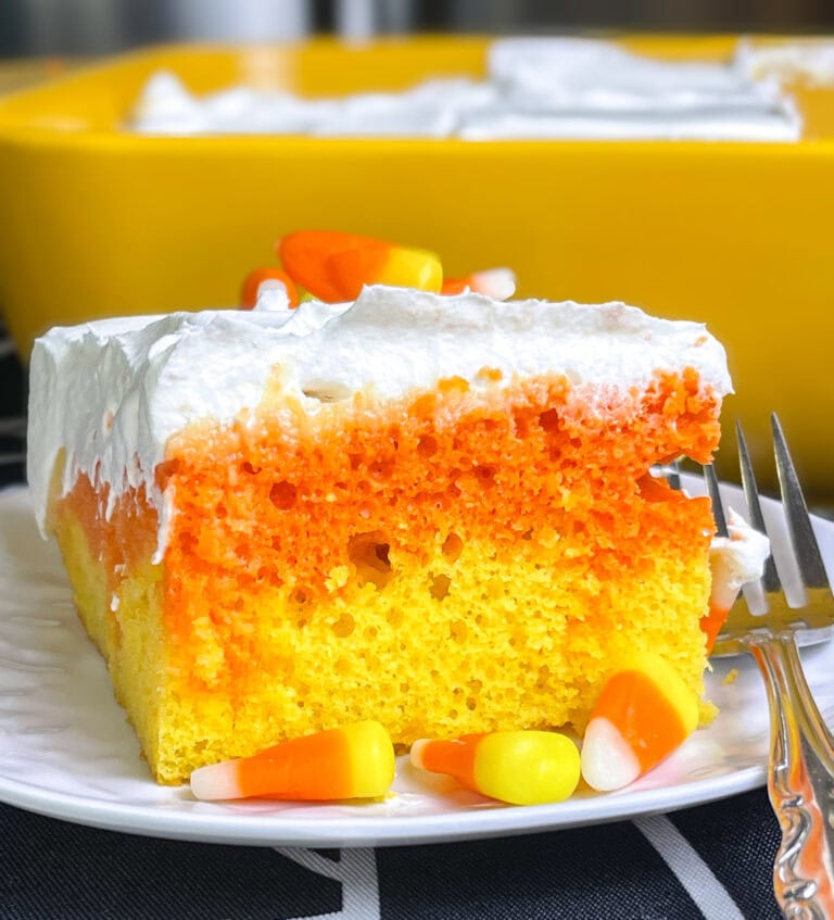 A festive candy corn poke cake in a 9x13 pan with layers of yellow and orange cake, topped with Cool Whip and decorated with candy corn pieces.