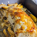 Sliced oven baked apple cider pork loin in a white baking dish surrounded by roasted apples, onions, and a golden cider glaze.