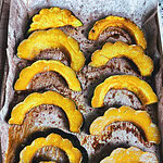 Golden maple roasted acorn squash slices arranged on a parchment-lined baking sheet, glistening with caramelized maple glaze and sprinkled with salted pumpkin seeds.