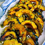 Golden maple roasted acorn squash slices arranged on a parchment-lined baking sheet, glistening with caramelized maple glaze and sprinkled with salted pumpkin seeds.