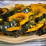 Golden maple roasted acorn squash slices arranged on a parchment-lined baking sheet, glistening with caramelized maple glaze and sprinkled with salted pumpkin seeds.